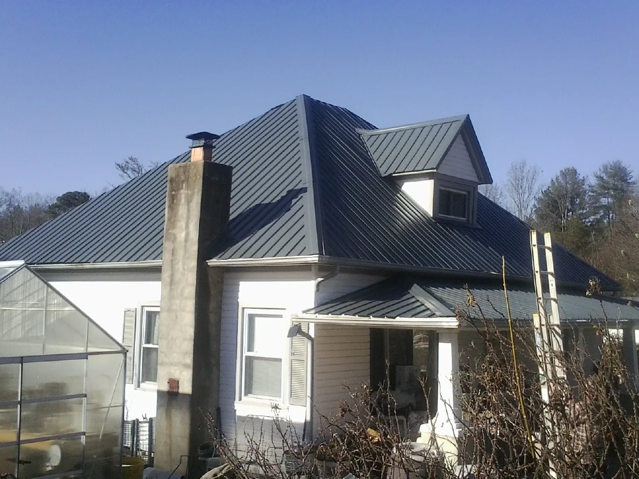 Dark blue standing seam metal roof on a white farmhouse with dormer — Slate & Tile Roof Repair by Roofing Brothers in Matlock