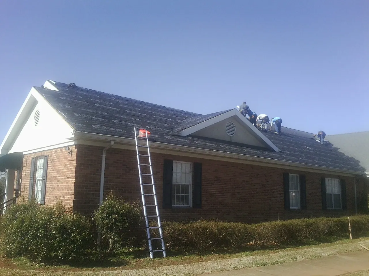 Crew tearing shingles off a brick ranch roof with a ladder set — Emergency Roof Repair work by our crew in Matlock