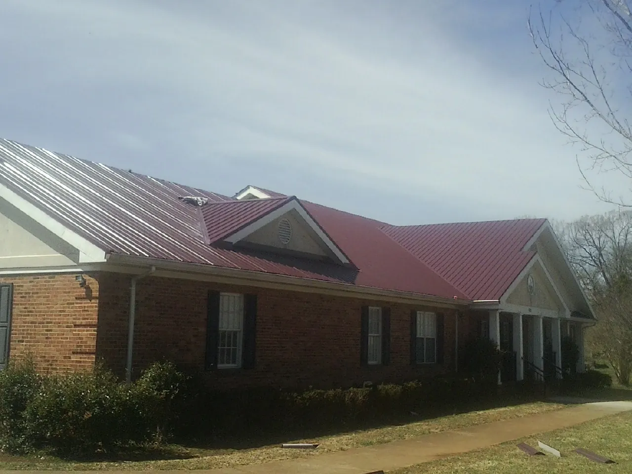 Red metal roof with gabled entries on a long brick building, from a Hail Damage Roof Repair job in Matlock