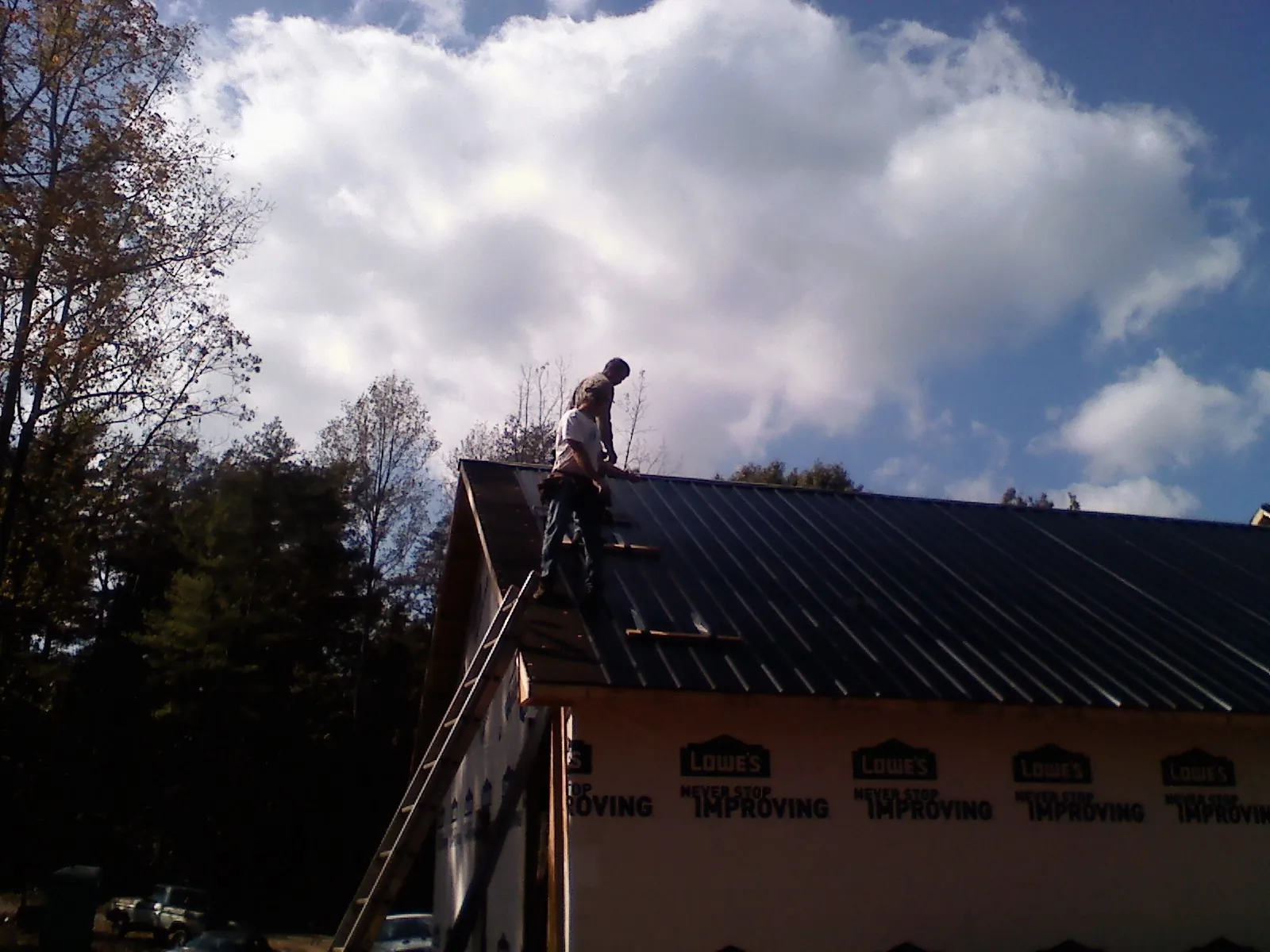 Roofer fastening dark metal panels high against a cloudy sky, from a Roof Inspection job in Matlock