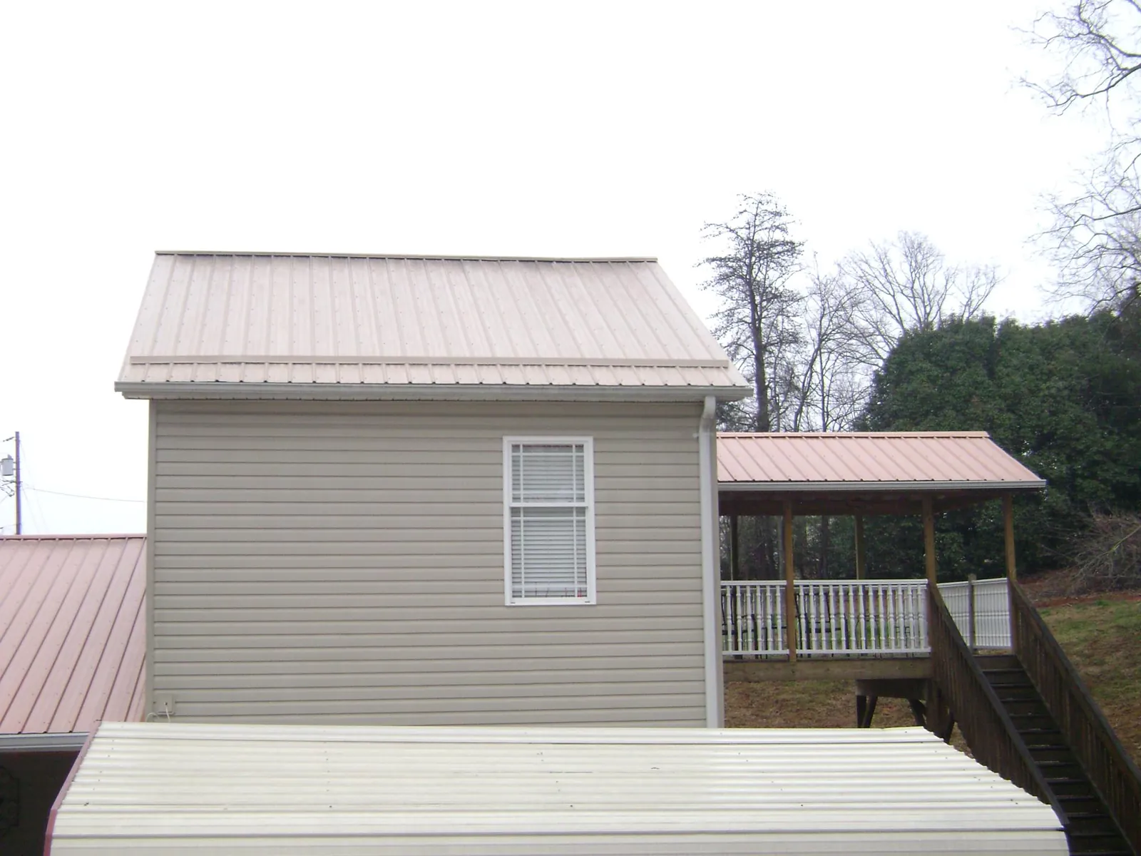 Tan metal roofs on a two story addition and attached porch, from a Roof Replacement job in Matlock